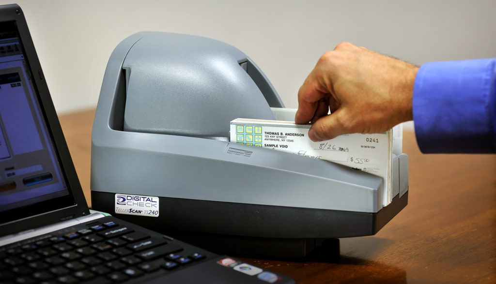 Teller capture scanner on desk with checks being inserted.
