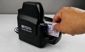 A hand inserting a driver's license into the front of a check scanner.